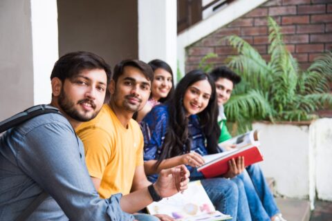young-asian-indian-college-students-reading-books-studying-laptop-preparing-exam-working-group-project-while-sitting-grass-staircase-steps-college-campus-min